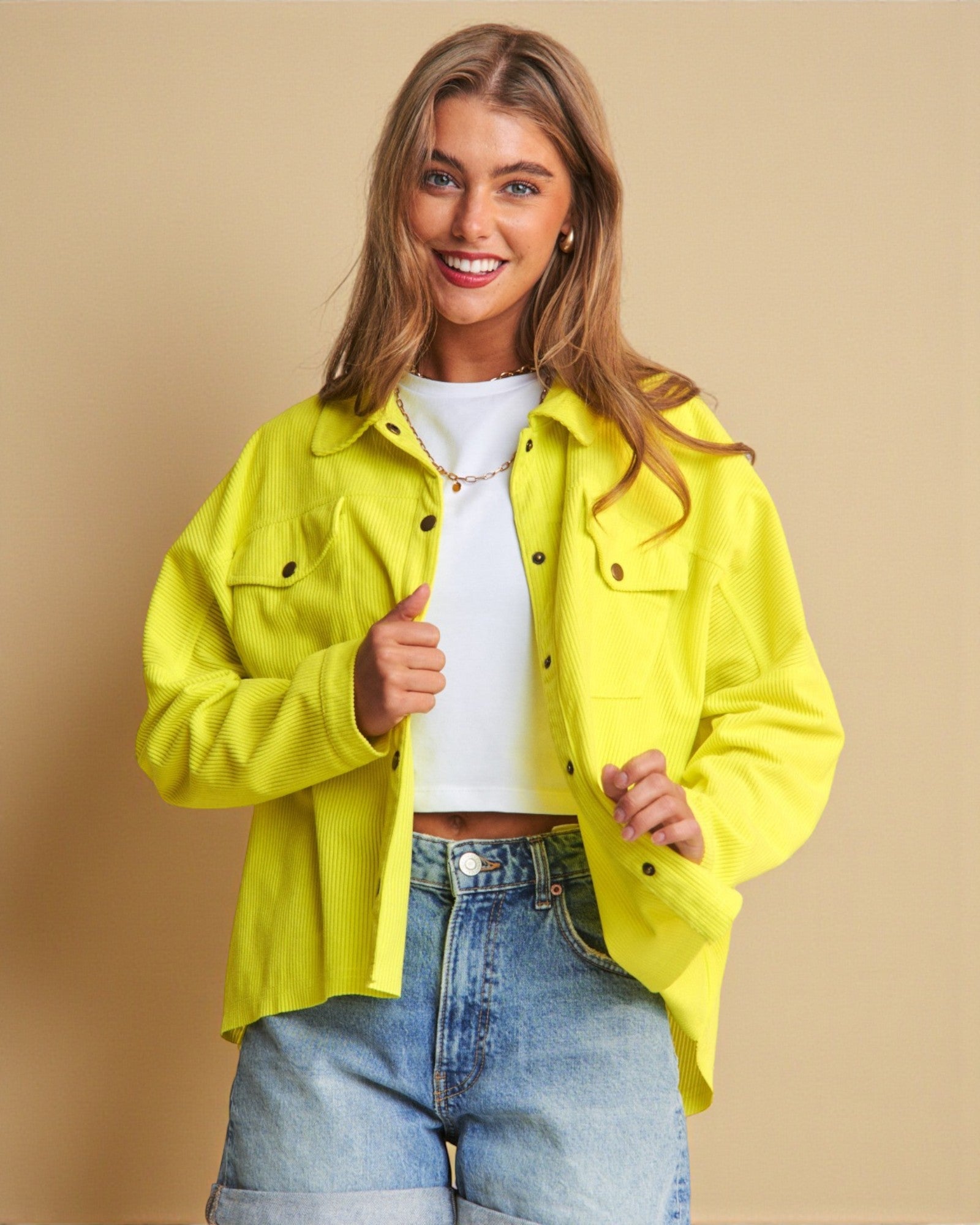 Woman wearing a bright yellow jacket over a white shirt and blue jeans on a beige background