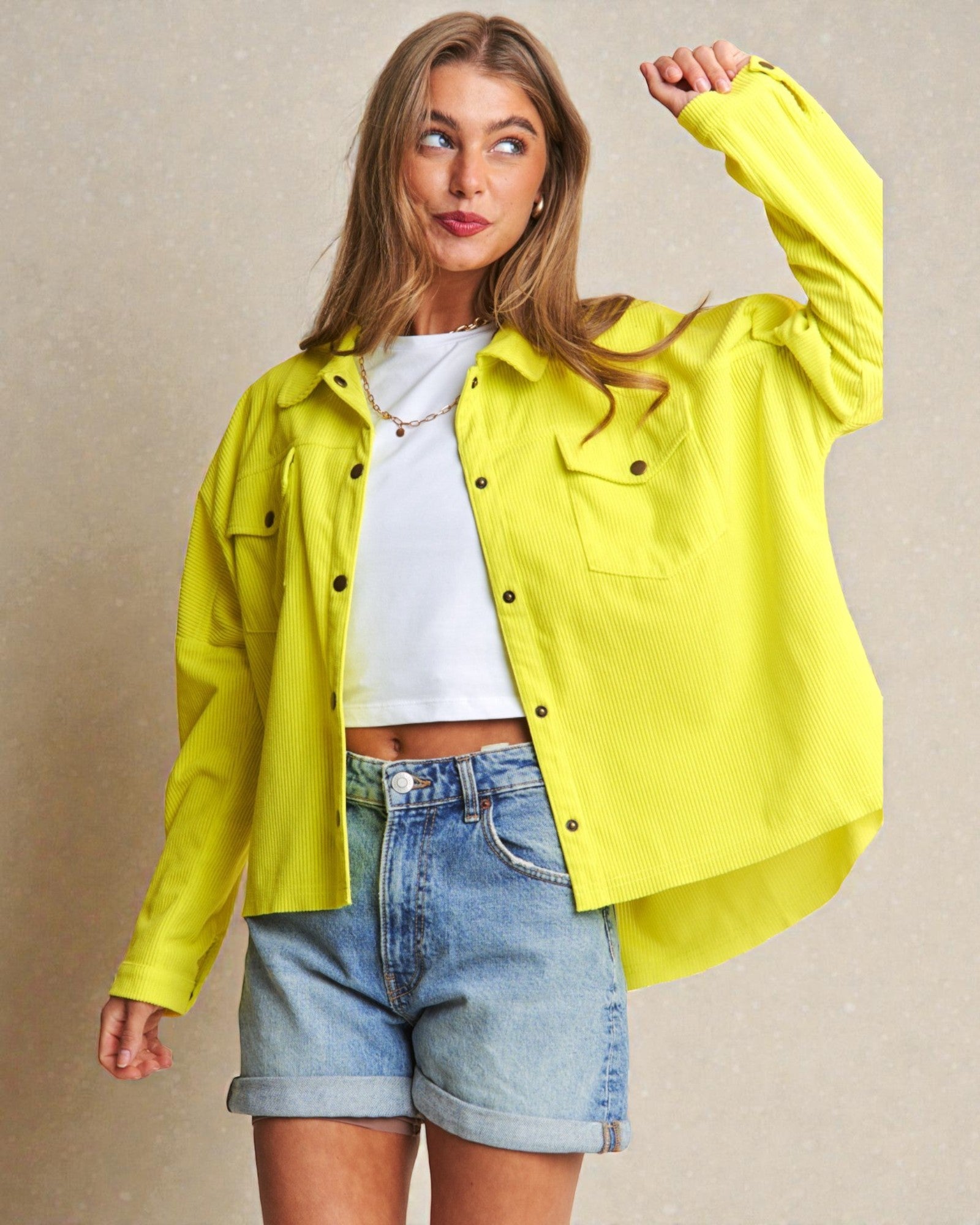 Woman wearing a bright yellow jacket over a white shirt and denim shorts on a beige background
