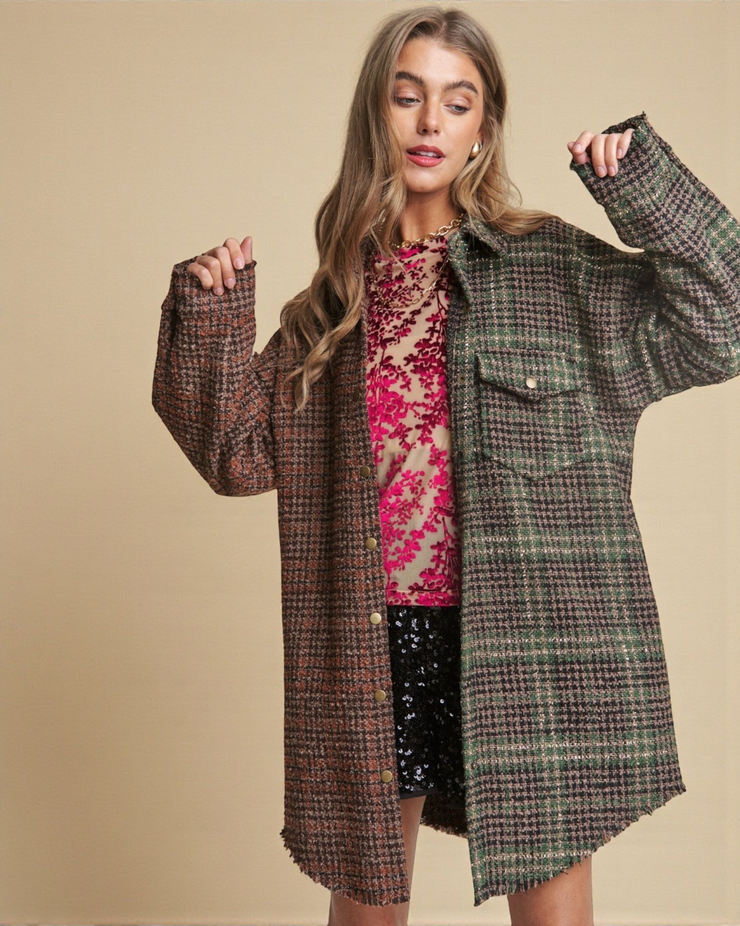 Woman wearing a plaid coat over a floral top and black skirt on a beige background