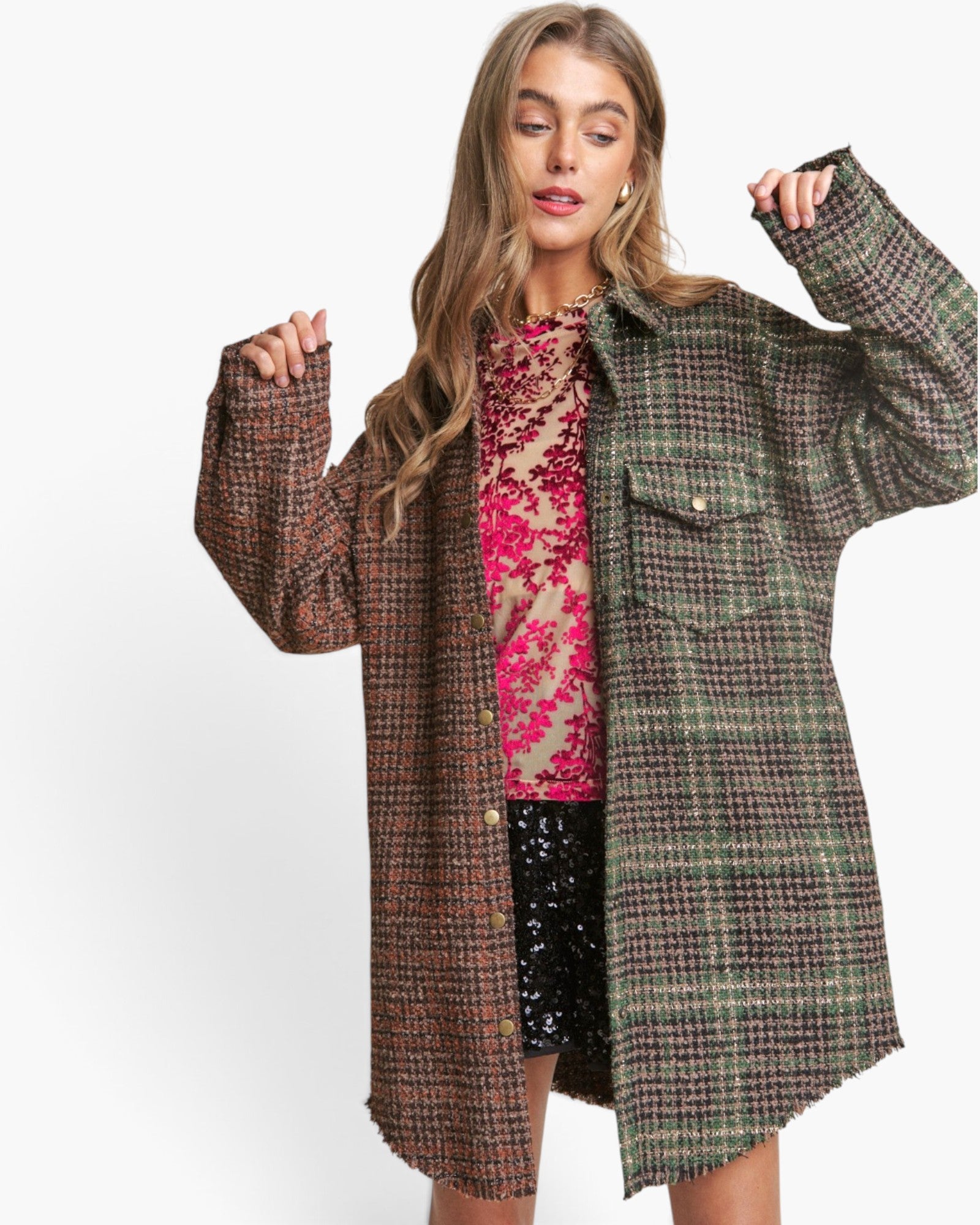A woman modeling a long, oversized plaid coat in brown, green, and black tweed over a pink sequined top and black sequined shorts, set against a plain white studio background.