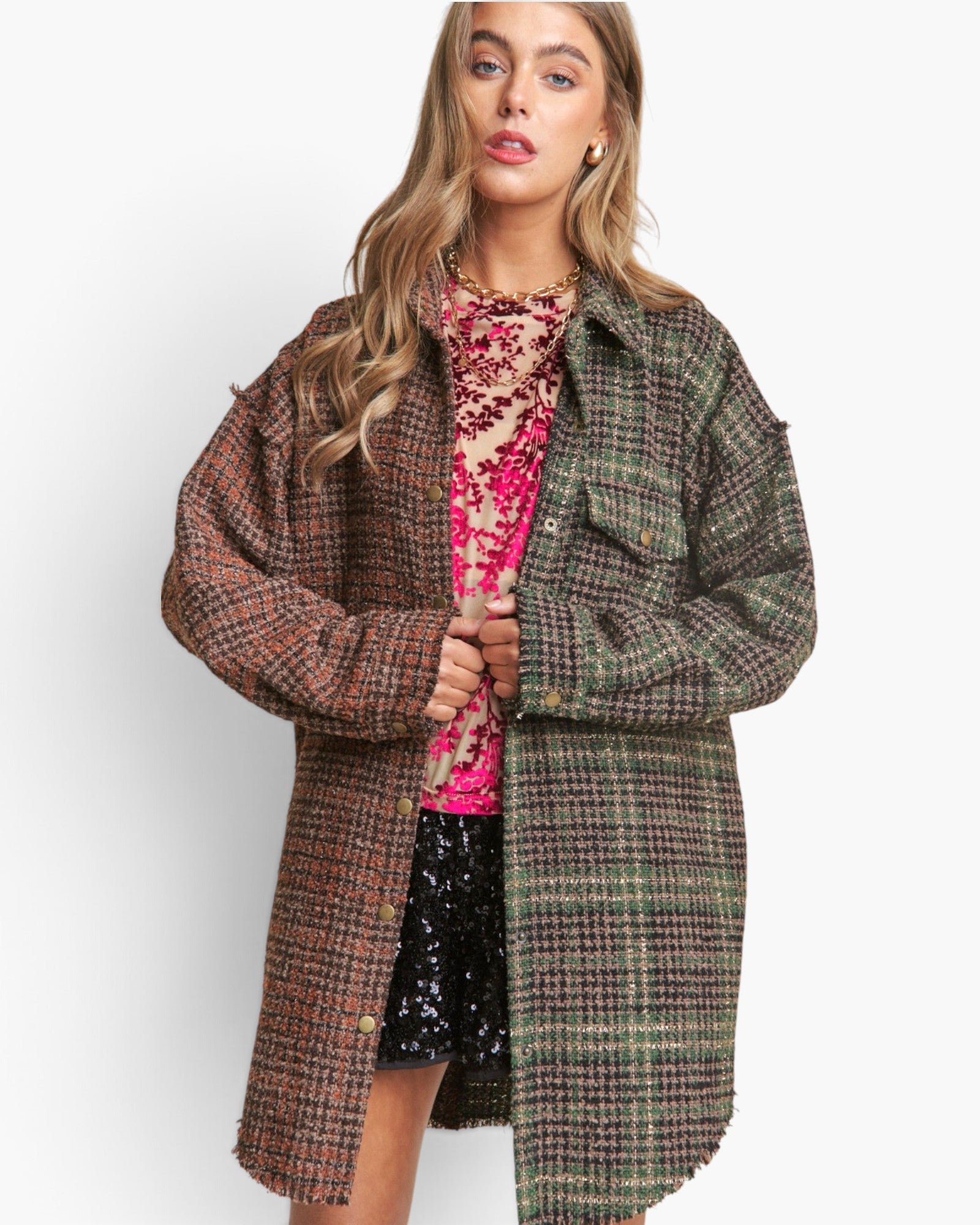 A woman modeling a long, oversized plaid coat with a brown and green tweed pattern, worn open over a pink sequined top and black sequined shorts, against a plain white background.