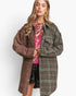 A woman modeling a long, oversized plaid coat with a brown and green tweed pattern, worn open over a pink sequined top and black sequined shorts, against a plain white background.