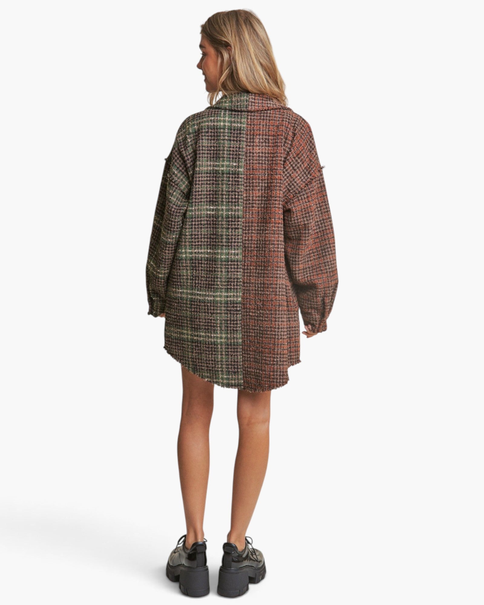 A woman shown from the back wearing an oversized plaid shirt dress in a brown, green, and red pattern, paired with black platform sneakers, against a light gray studio background.