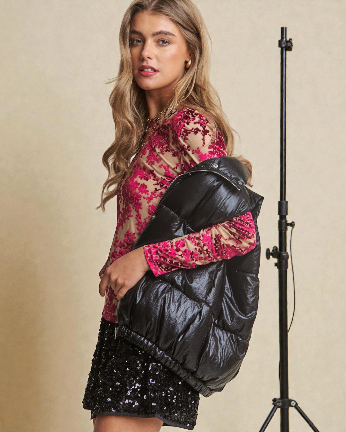 Woman wearing a black puffer jacket over a pink floral top with a beige background