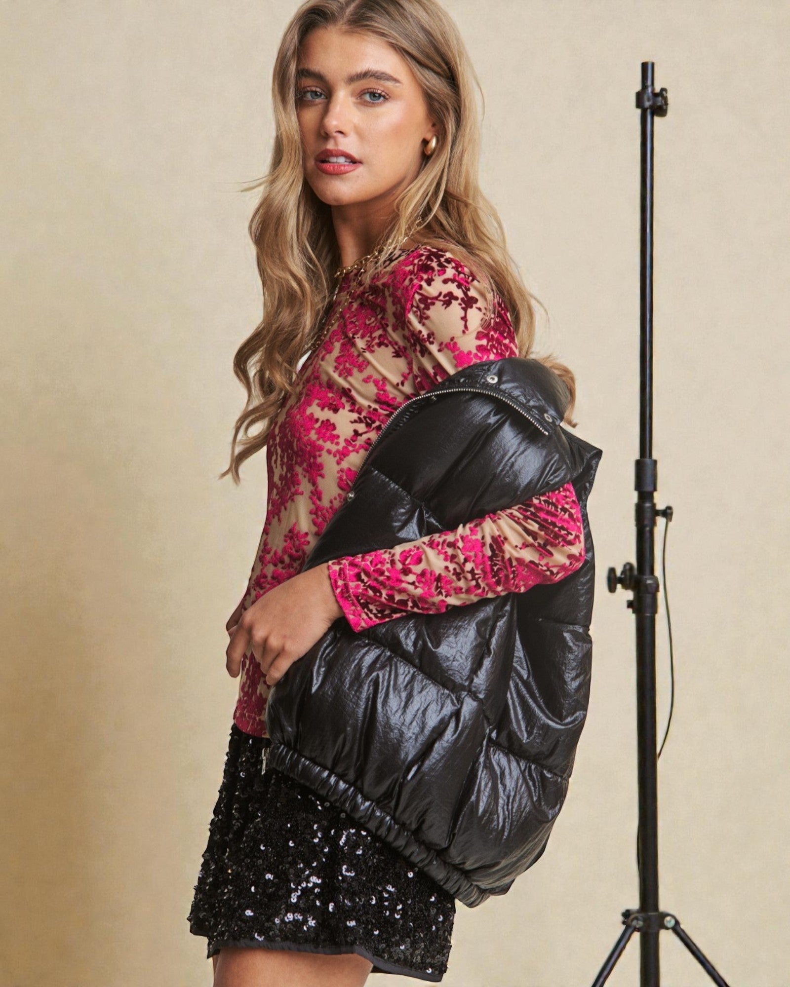 Woman wearing a black puffer jacket over a pink floral top with a beige background