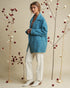 Woman wearing a blue coat standing between decorative plants with red berries on a beige background