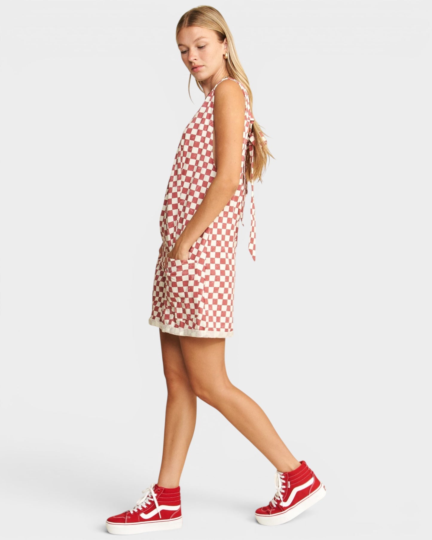 Woman wearing a red and white checkered dress with red high-top sneakers on a light gray background