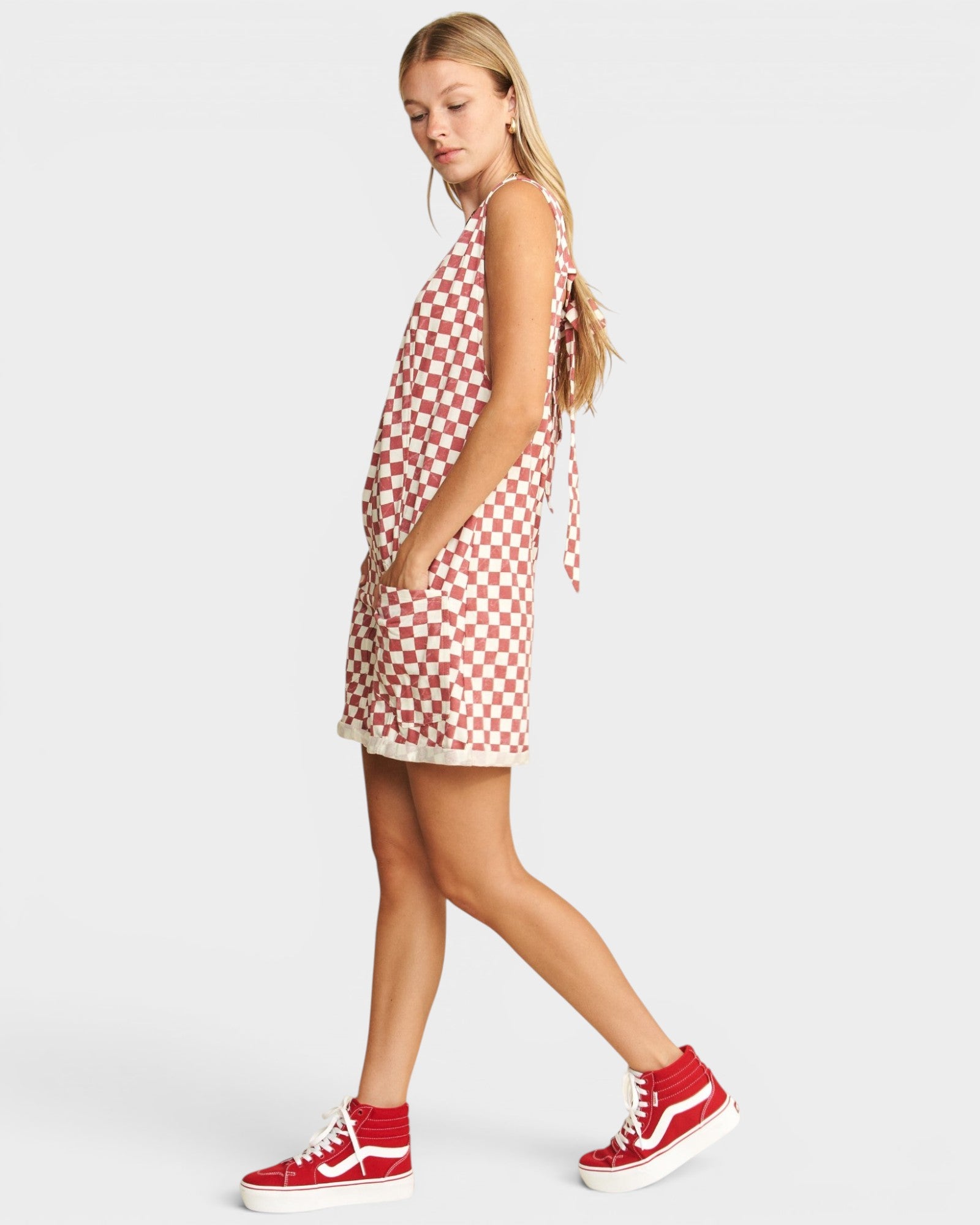 Woman wearing a red and white checkered dress with red high-top sneakers on a light gray background