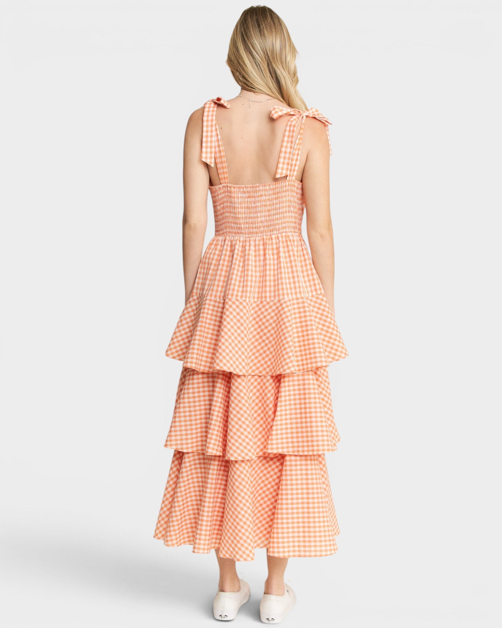 Woman wearing a peach gingham dress with tiered layers on a white background