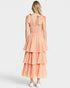 Woman wearing a peach gingham dress with tiered layers on a white background
