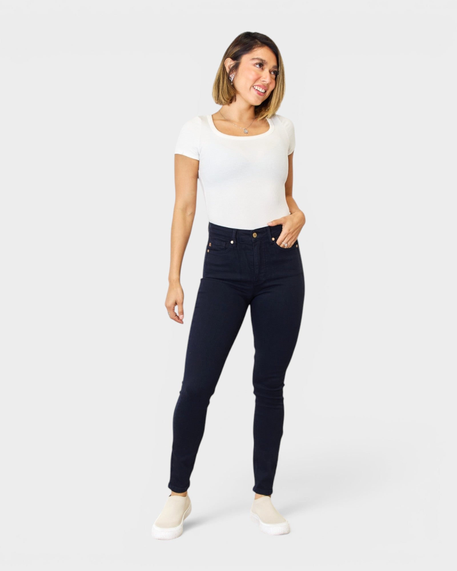 Woman wearing navy blue jeans and a white top on a white background