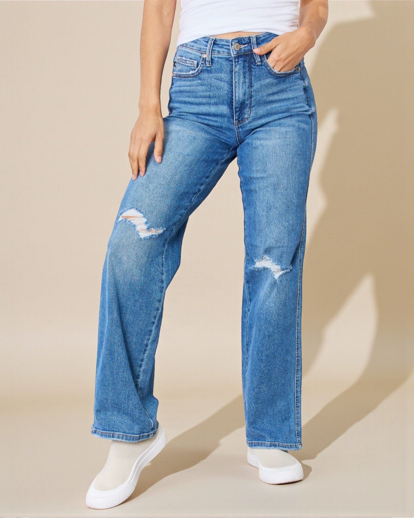 Person wearing blue jeans with slight distressing on a beige background