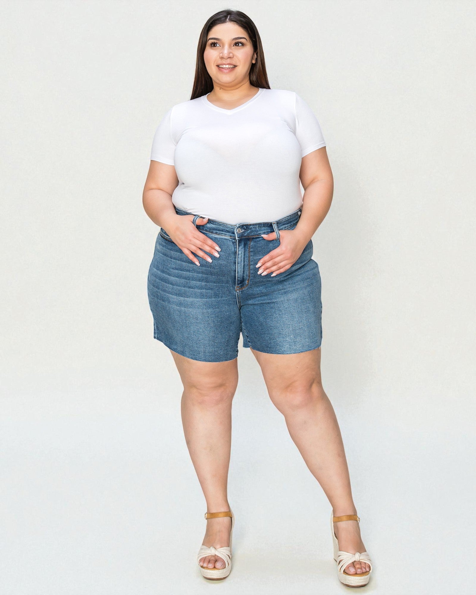 Woman wearing a white t-shirt and blue denim shorts on a plain background
