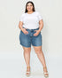Woman wearing a white t-shirt and blue denim shorts on a plain background
