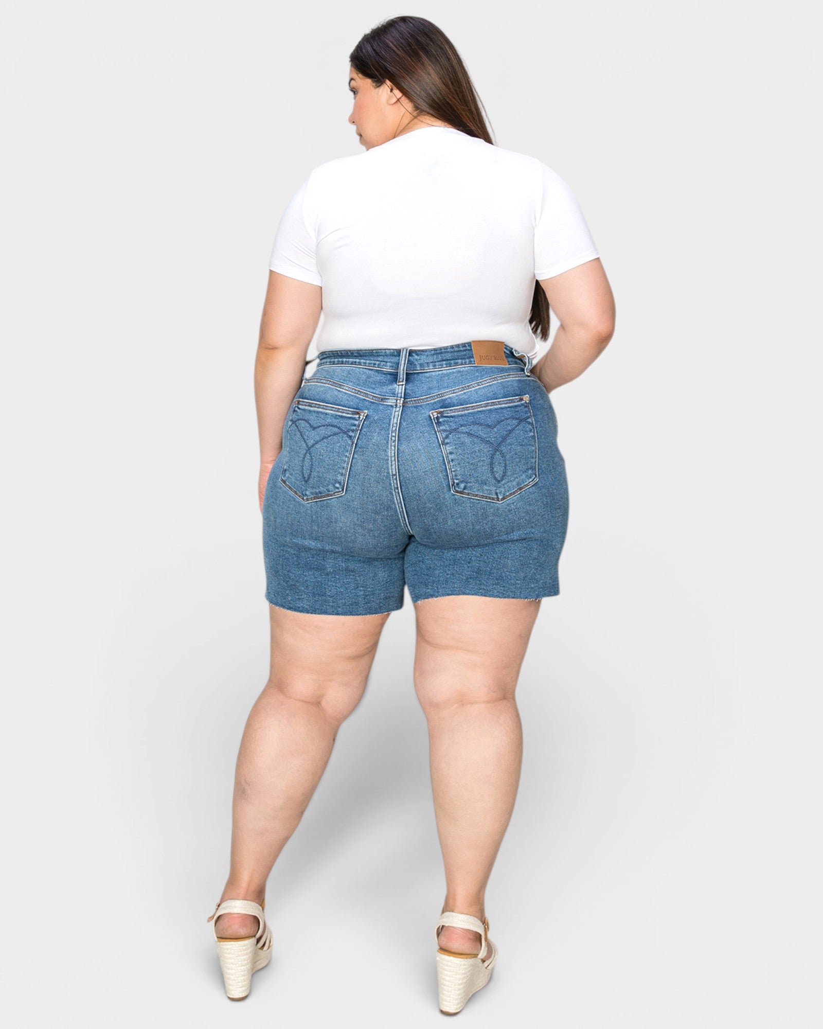 Person wearing blue denim shorts and a white t-shirt on a plain background