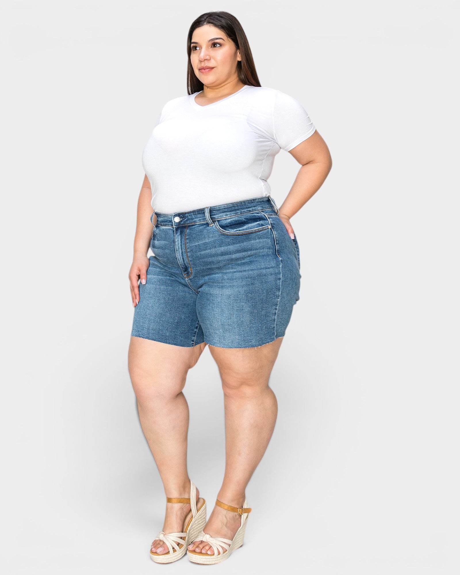 Woman wearing a white t-shirt and blue denim shorts on a plain background