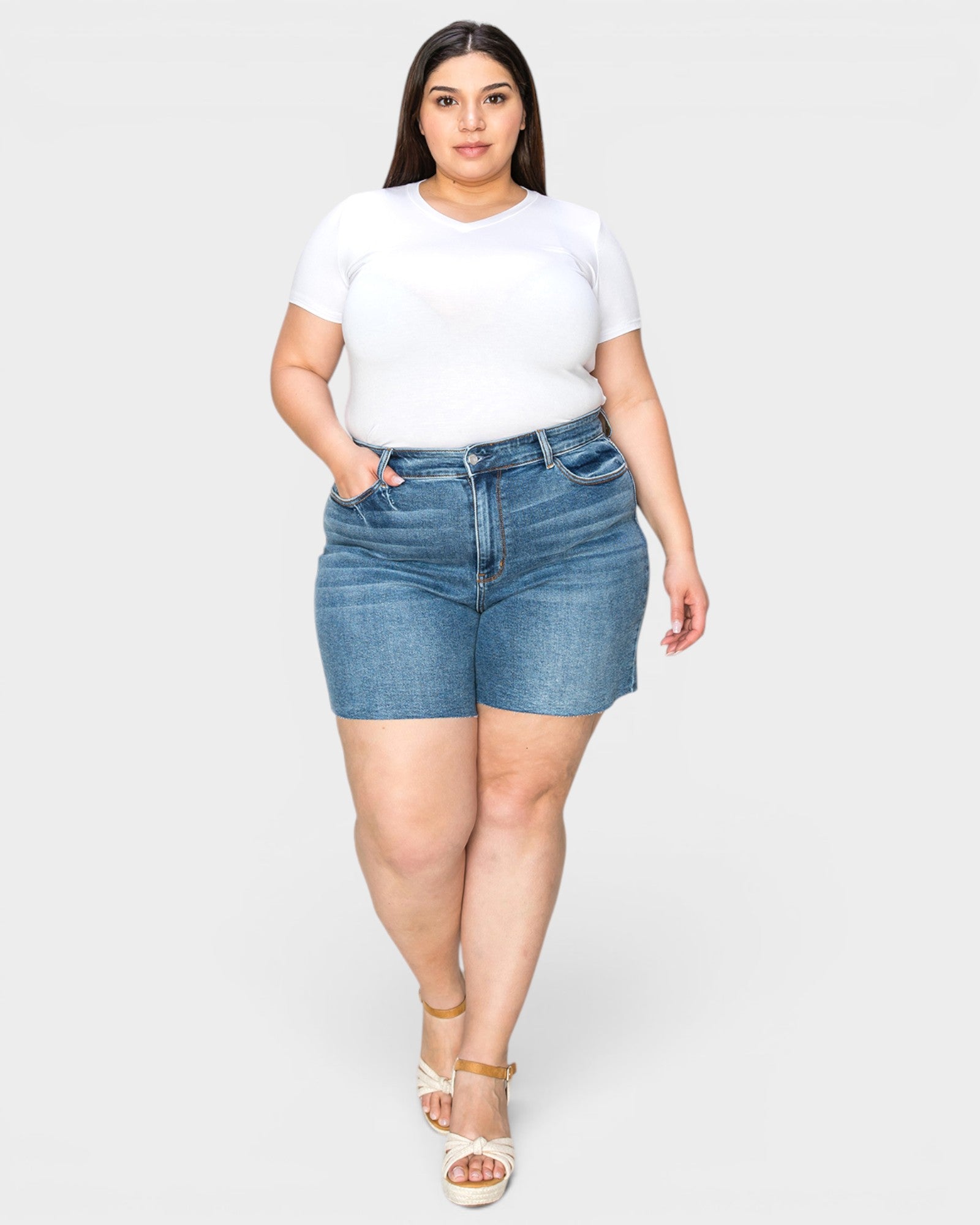 Woman wearing a white t-shirt and blue denim shorts on a plain background