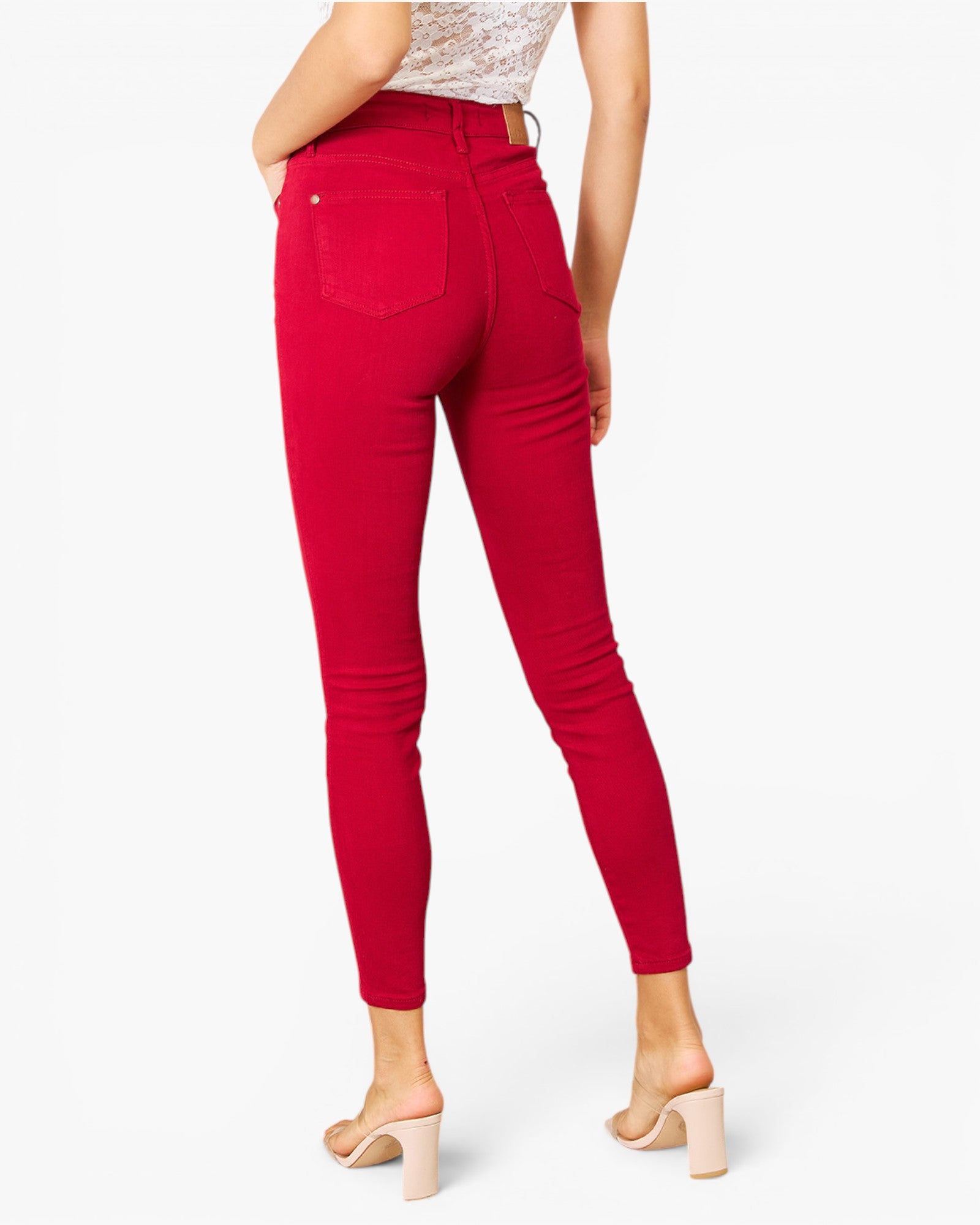 A model shown from the back wearing bright red skinny jeans, a white patterned top, and beige block-heel mule sandals against a plain white studio background.