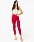 A woman modeling bright red skinny jeans with a white lace-trim camisole top, standing against a plain white studio background.
