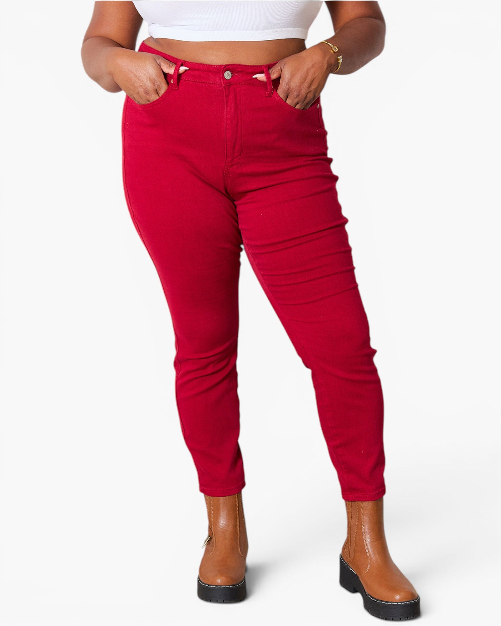 A model wearing bright red high-waisted skinny jeans with a ruched side detail, paired with a white crop top and brown platform ankle boots, against a plain white background.