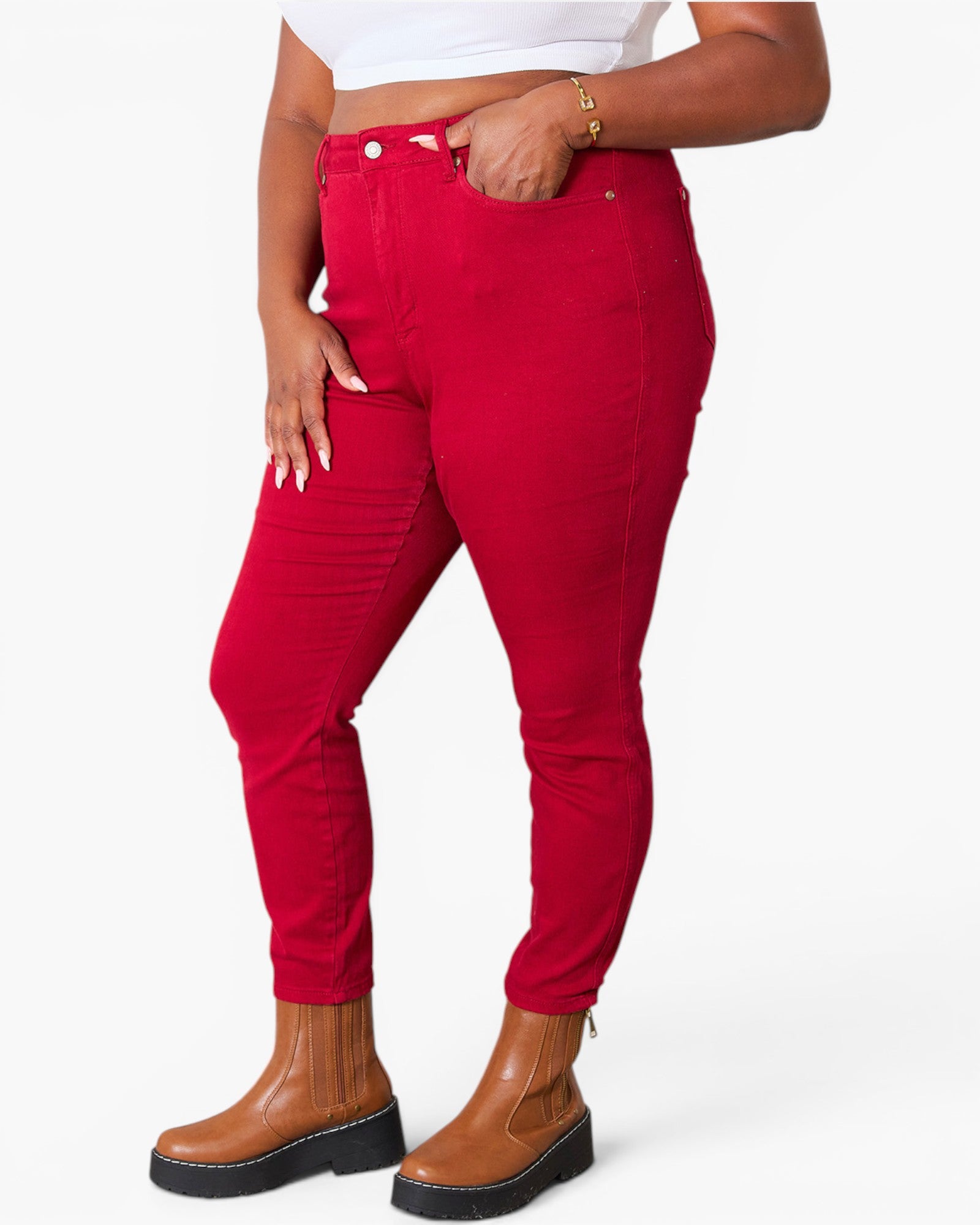 A model wearing bright red high-waisted ankle-length skinny jeans with zippered ankle cuffs, paired with brown platform ankle boots against a plain white studio background.