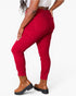 A model wearing bright red high-waisted ankle-length skinny jeans with brown platform ankle boots, shown from a side-back angle against a plain white studio background.