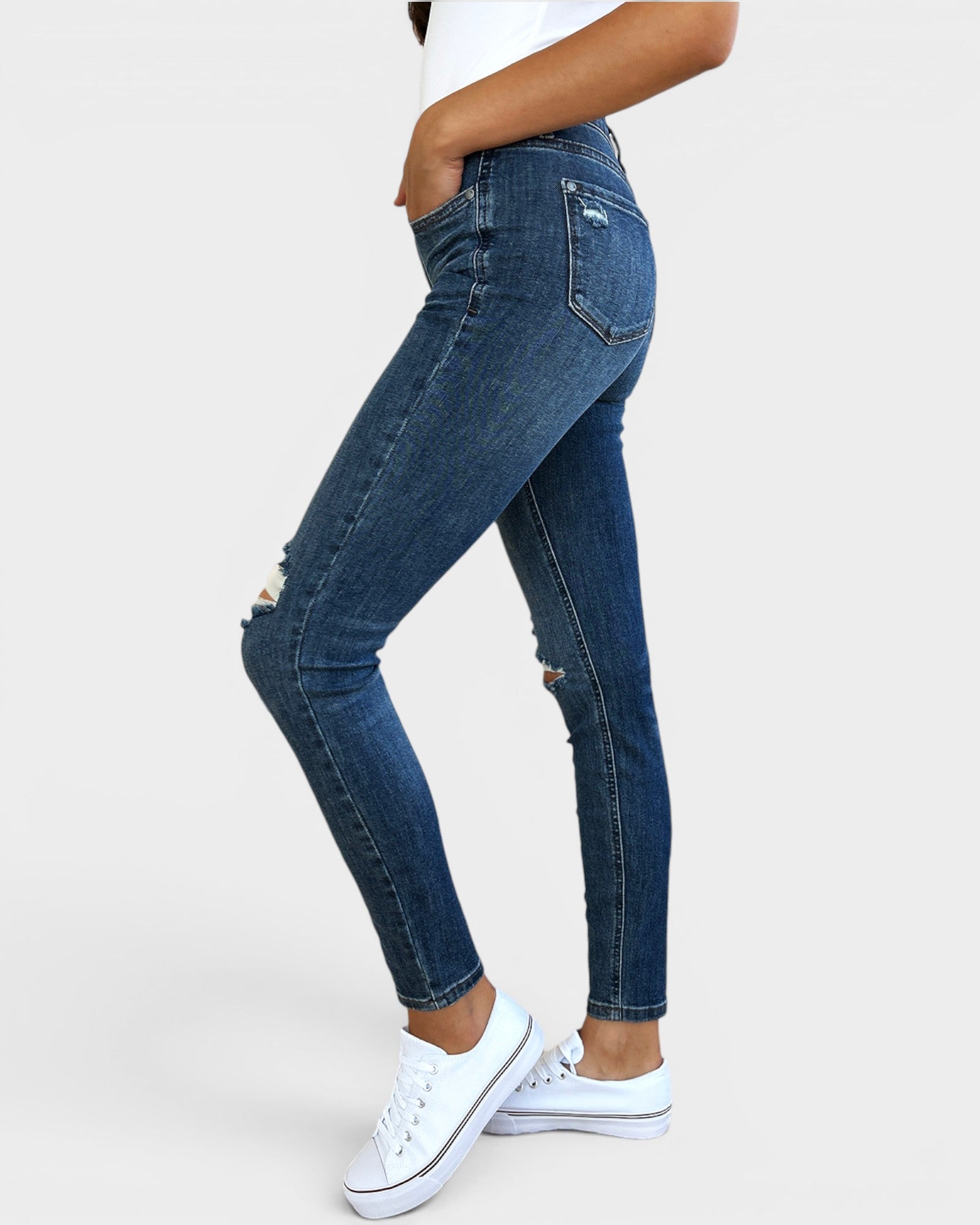 Person wearing blue jeans and white sneakers on a plain background