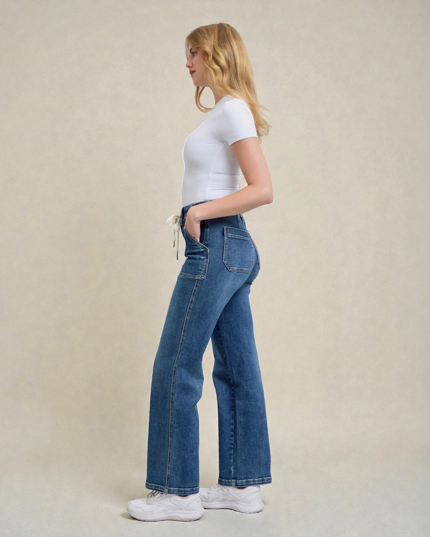 Woman wearing blue jeans and a white t-shirt on a beige background