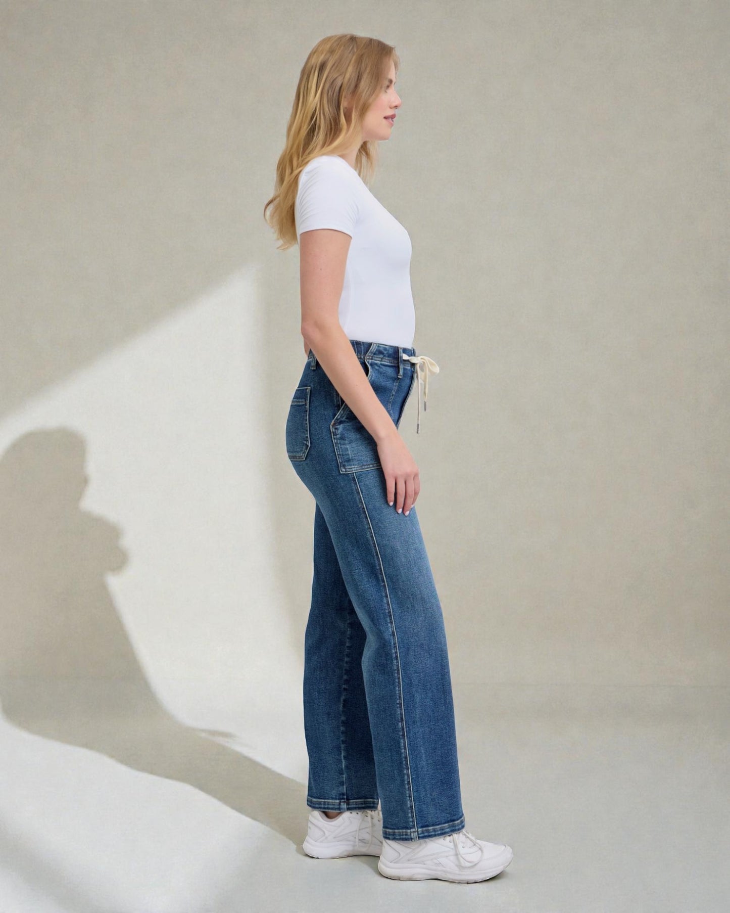 Woman wearing blue jeans and a white t-shirt against a plain background
