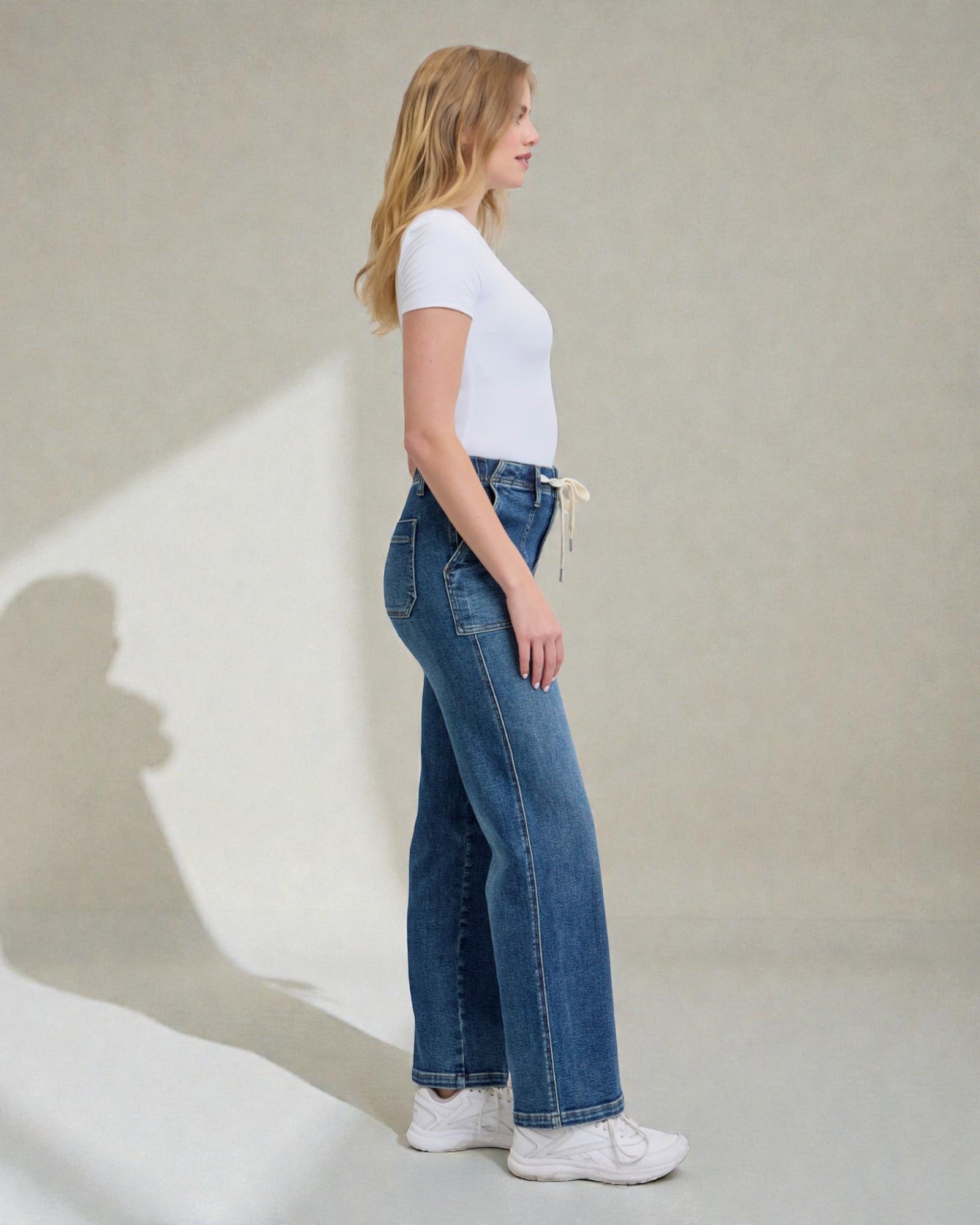 Woman wearing blue jeans and a white t-shirt against a plain background