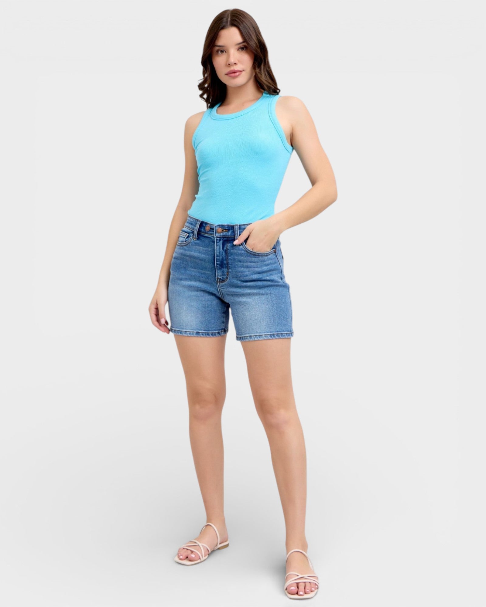 Woman wearing a light blue sleeveless top and denim shorts on a white background
