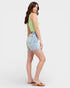 Woman wearing a light green sleeveless top and denim shorts on a white background