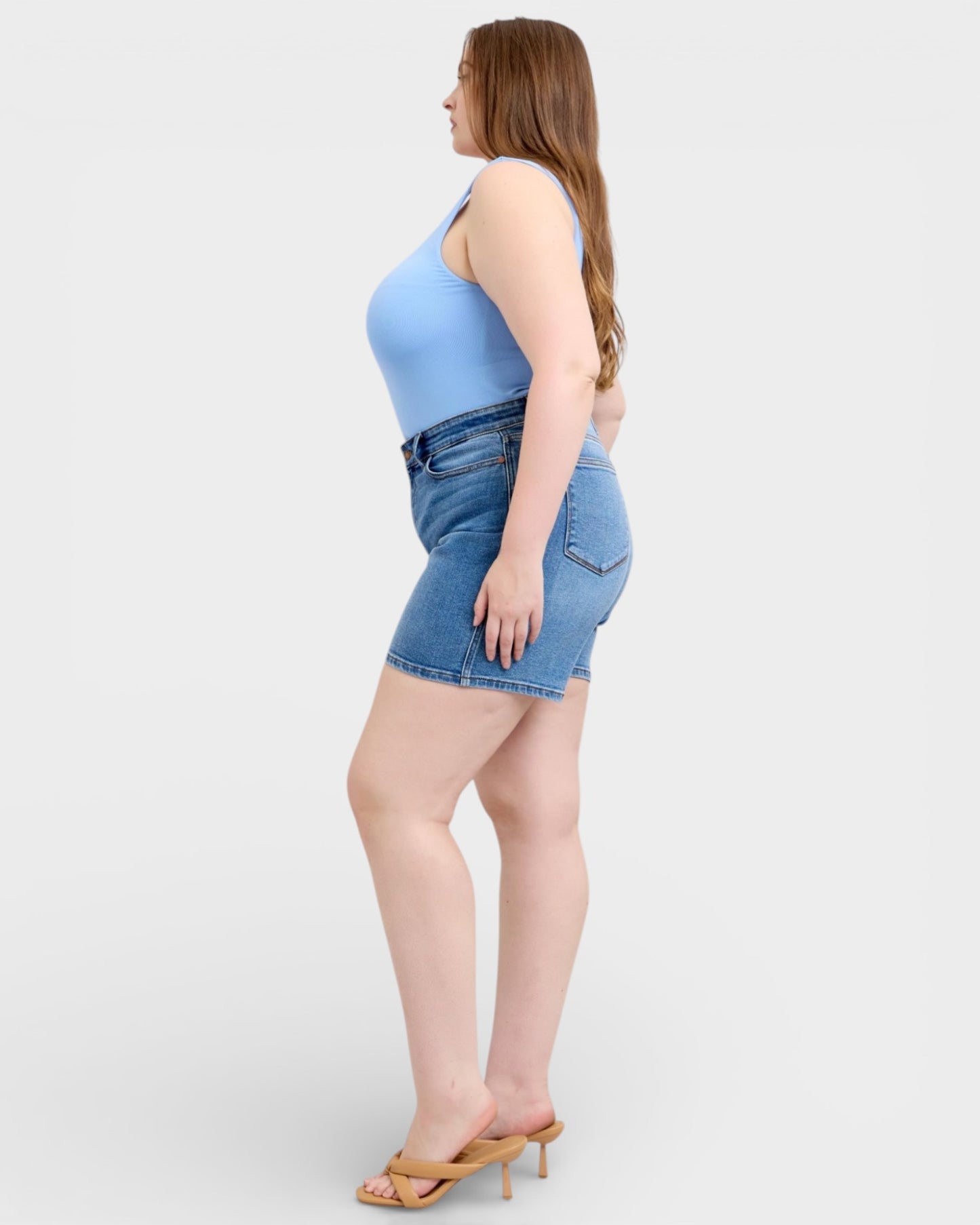 Woman wearing a light blue tank top and denim shorts on a white background
