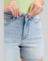 Light blue denim shorts being adjusted on a plain background