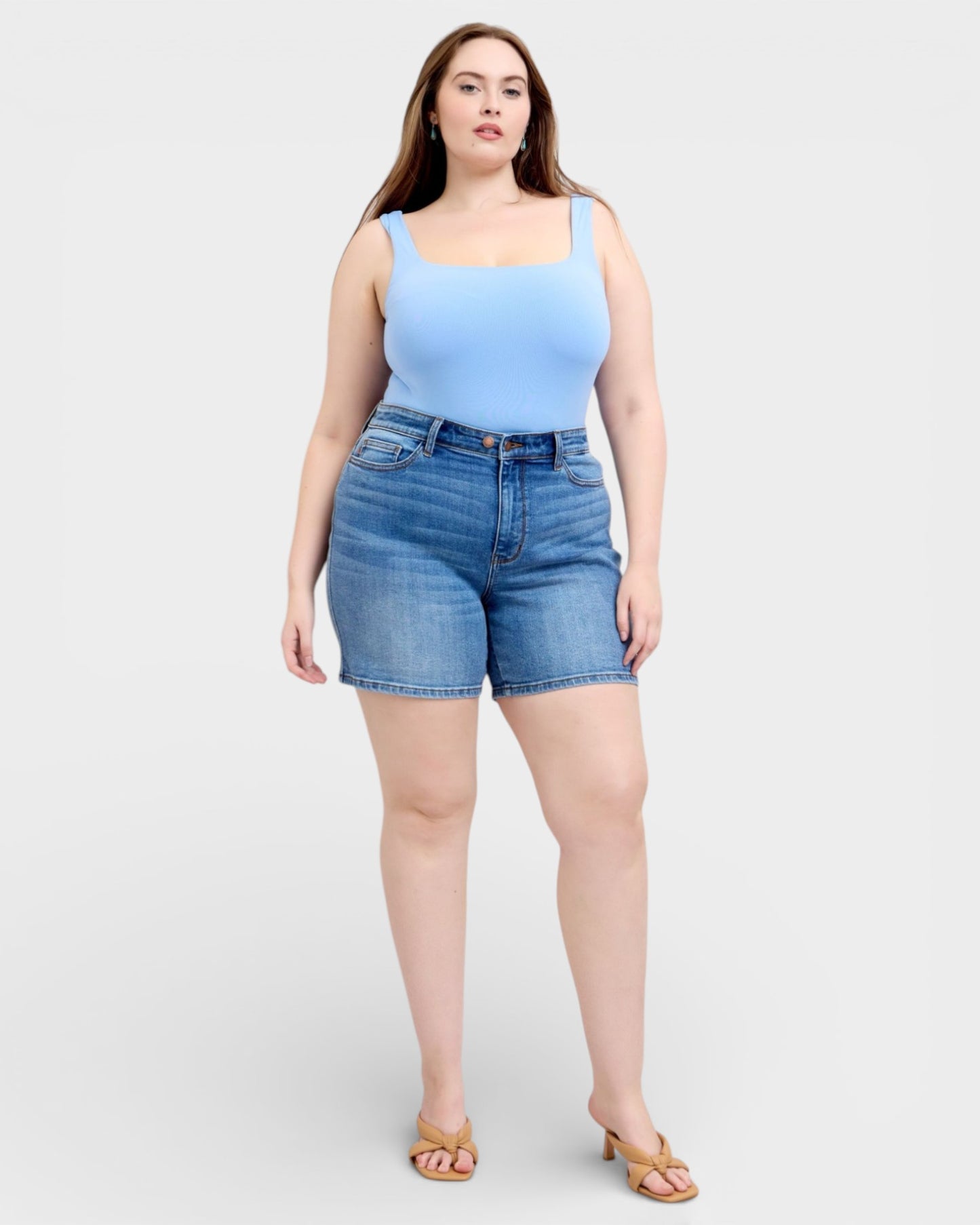 Woman wearing a light blue tank top and denim shorts on a white background