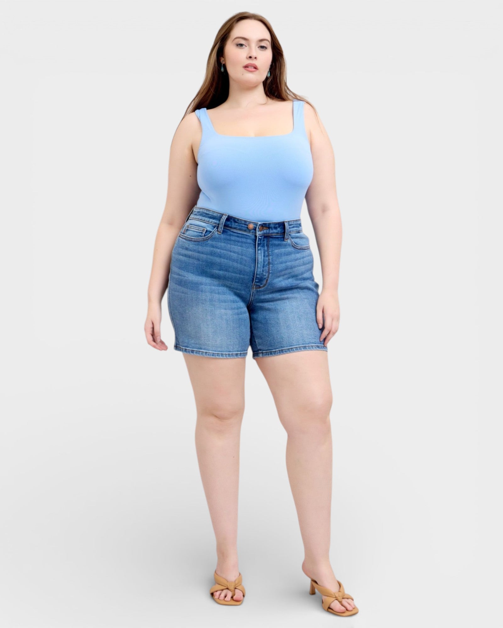 Woman wearing a light blue tank top and denim shorts on a white background
