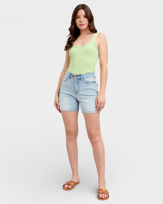 Woman wearing a light green tank top and denim shorts on a white background
