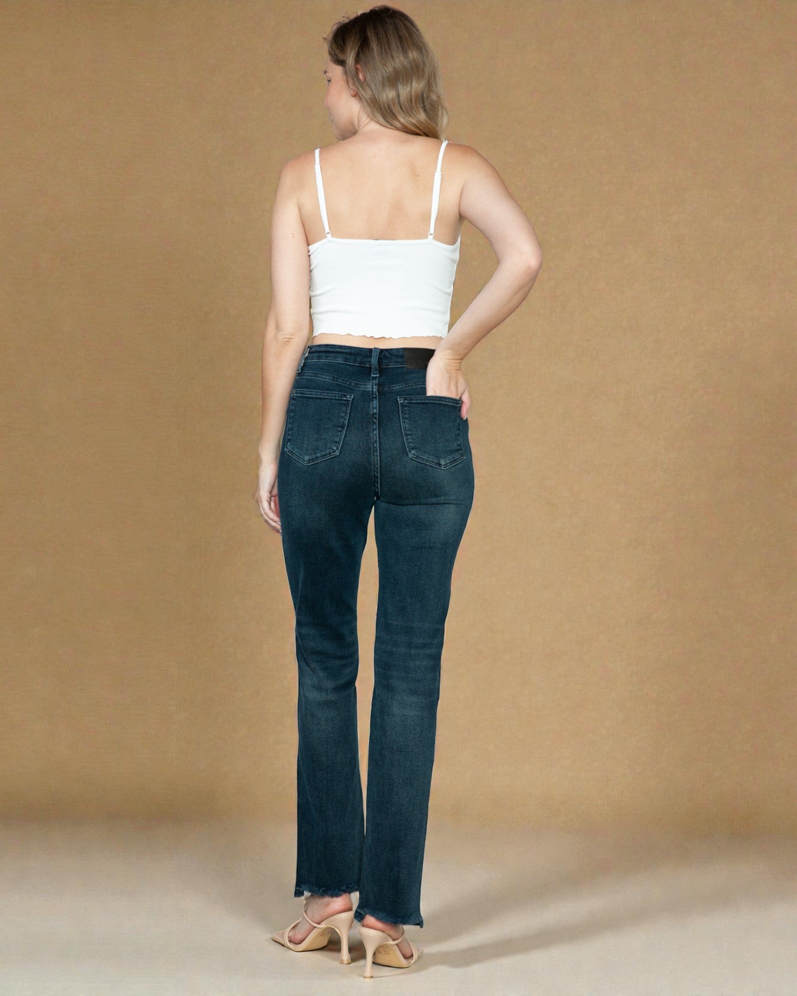Woman wearing dark blue jeans and a white top against a beige background