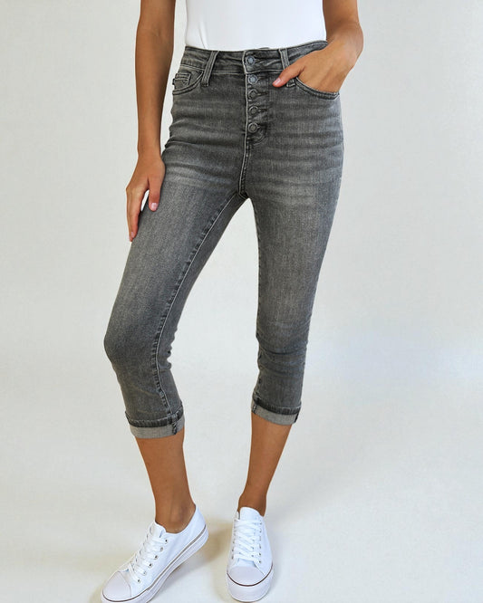 Person wearing gray capri jeans and white sneakers on a plain background