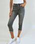 Person wearing gray capri jeans and white sneakers on a plain background
