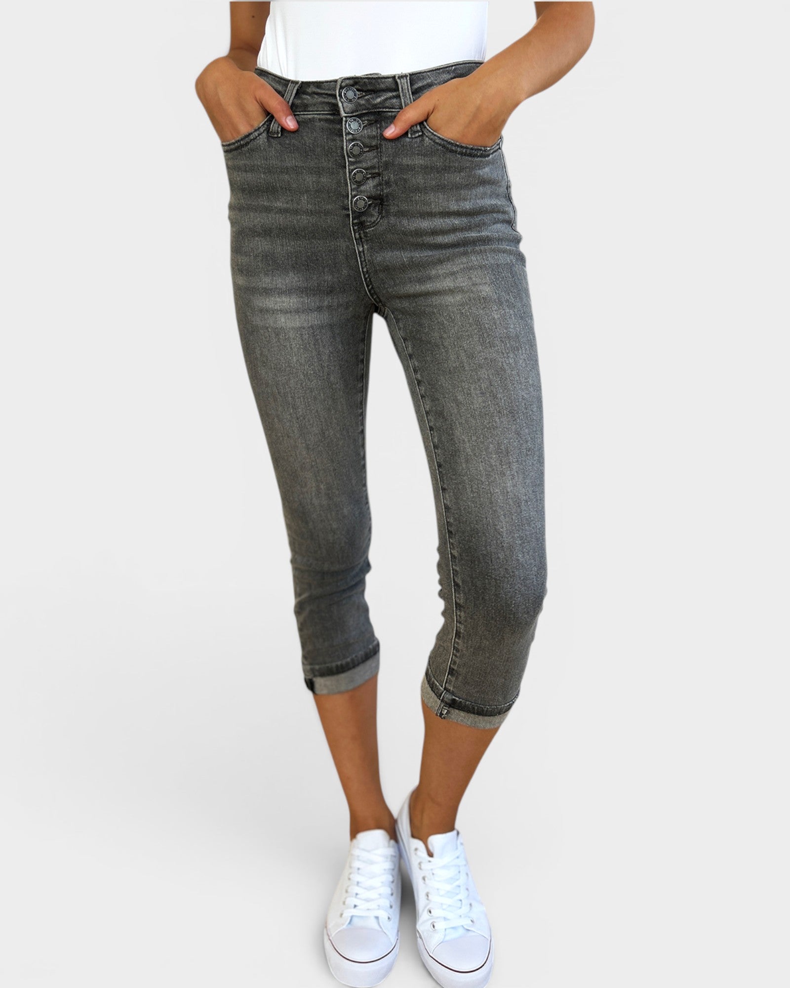 Person wearing gray jeans and white sneakers on a plain background
