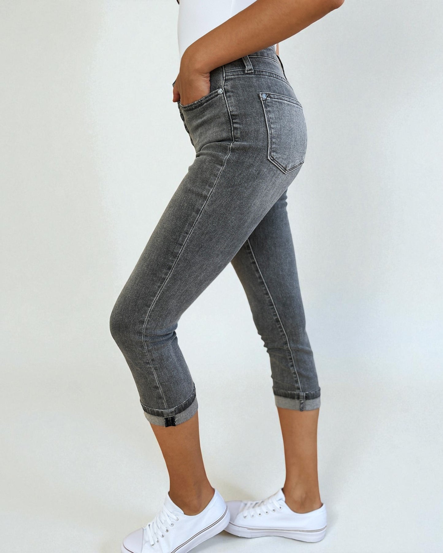 Person wearing gray jeans and white sneakers on a plain background