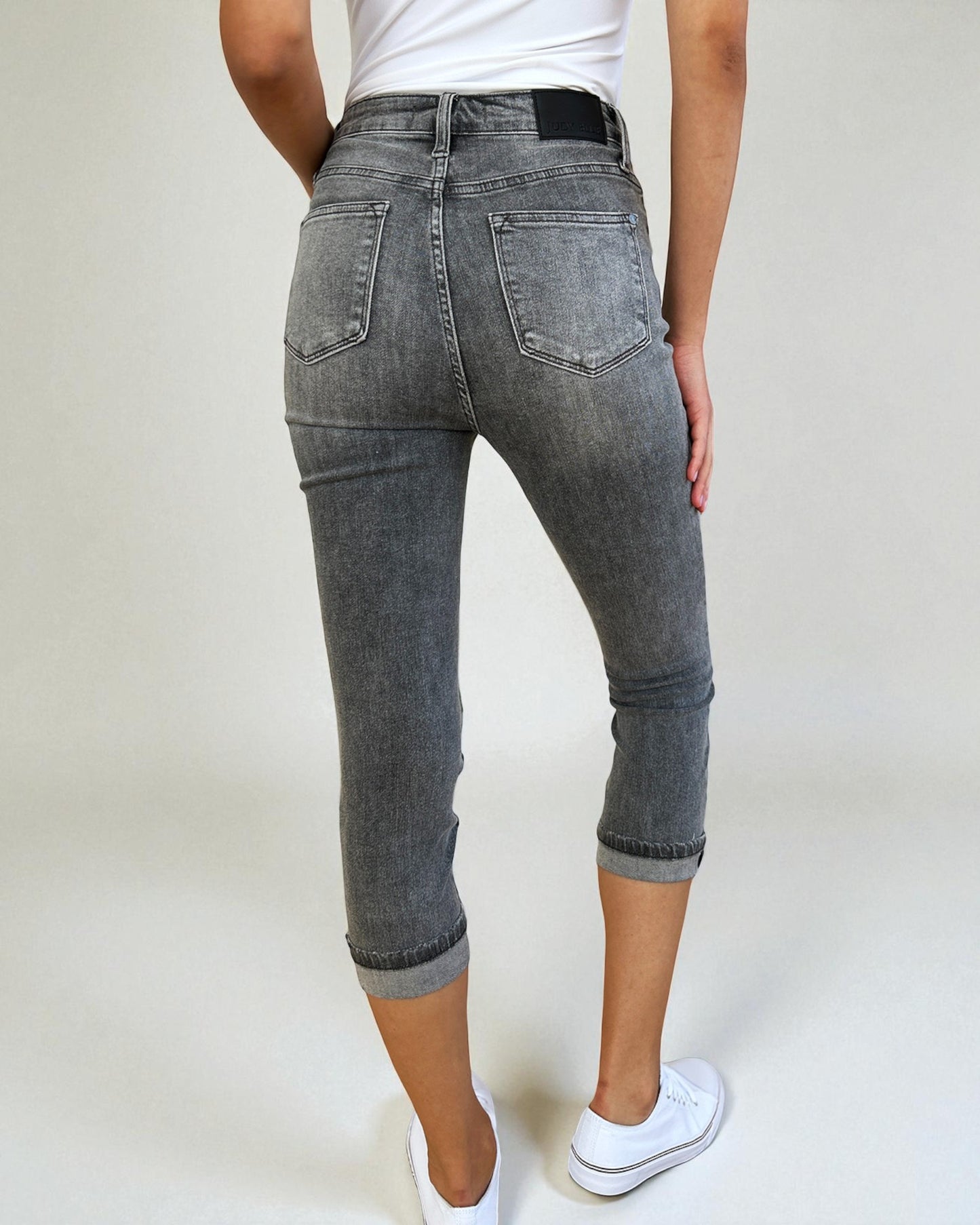 Person wearing gray jeans and white sneakers on a plain background