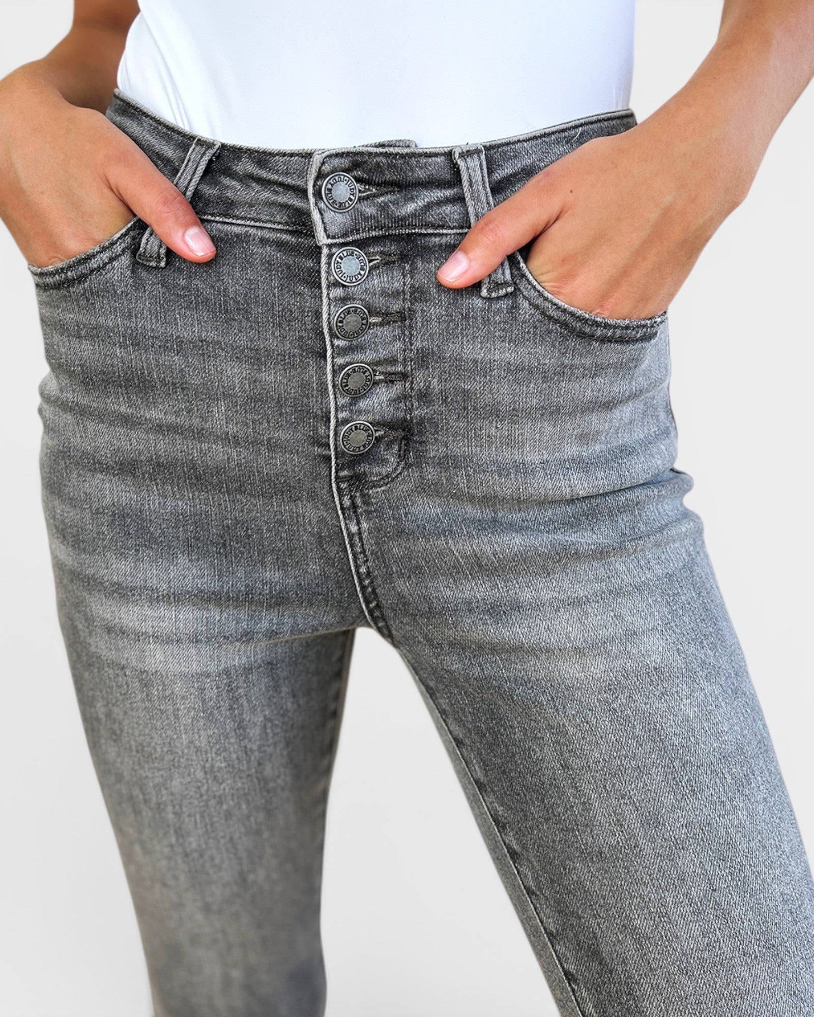 Gray jeans with button details worn by a person on a plain background