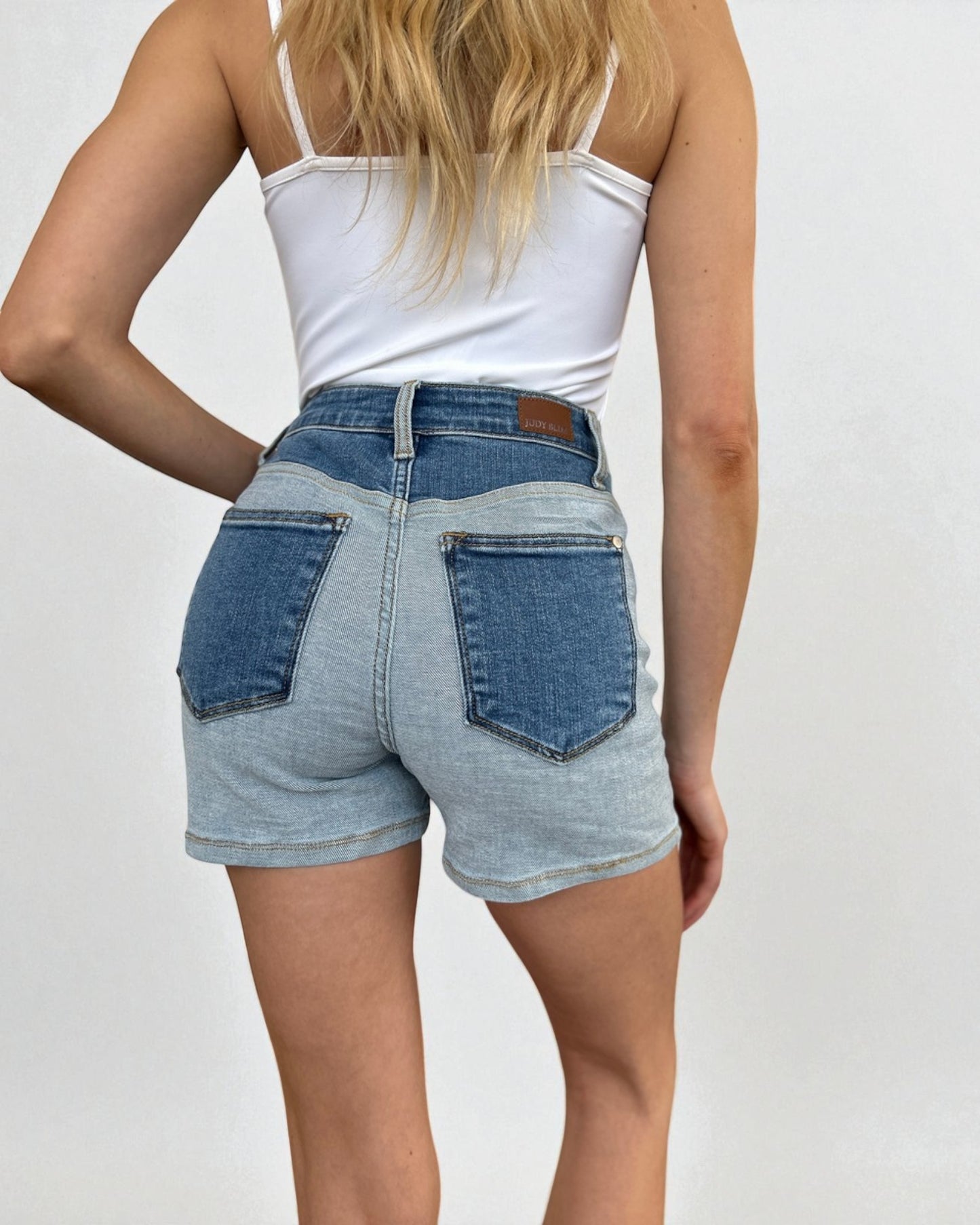 Person wearing a white tank top and blue denim shorts on a plain background