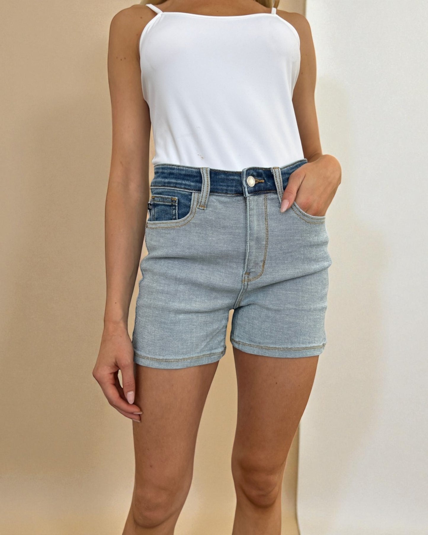 Person wearing a white top and blue denim shorts against a beige background