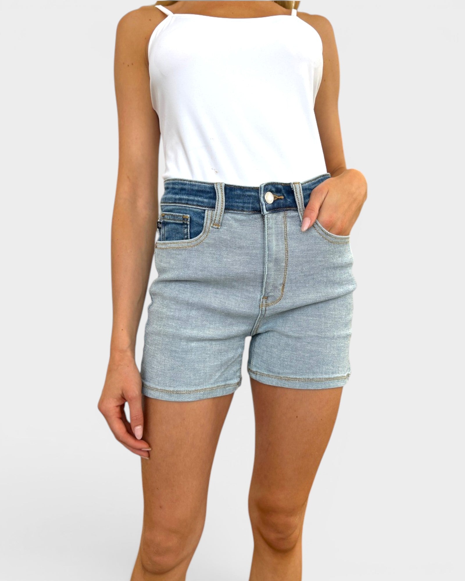 Person wearing light blue denim shorts and a white tank top on a plain background