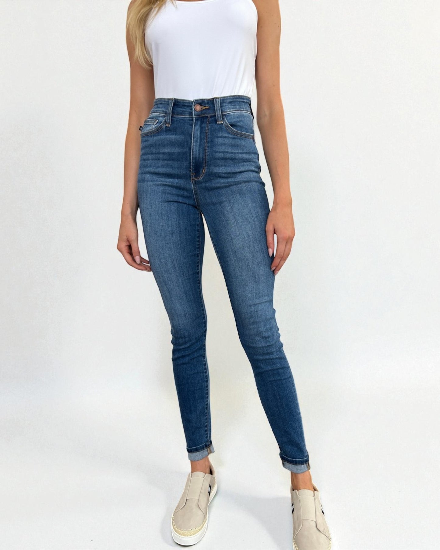 Person wearing blue jeans and a white top on a plain background