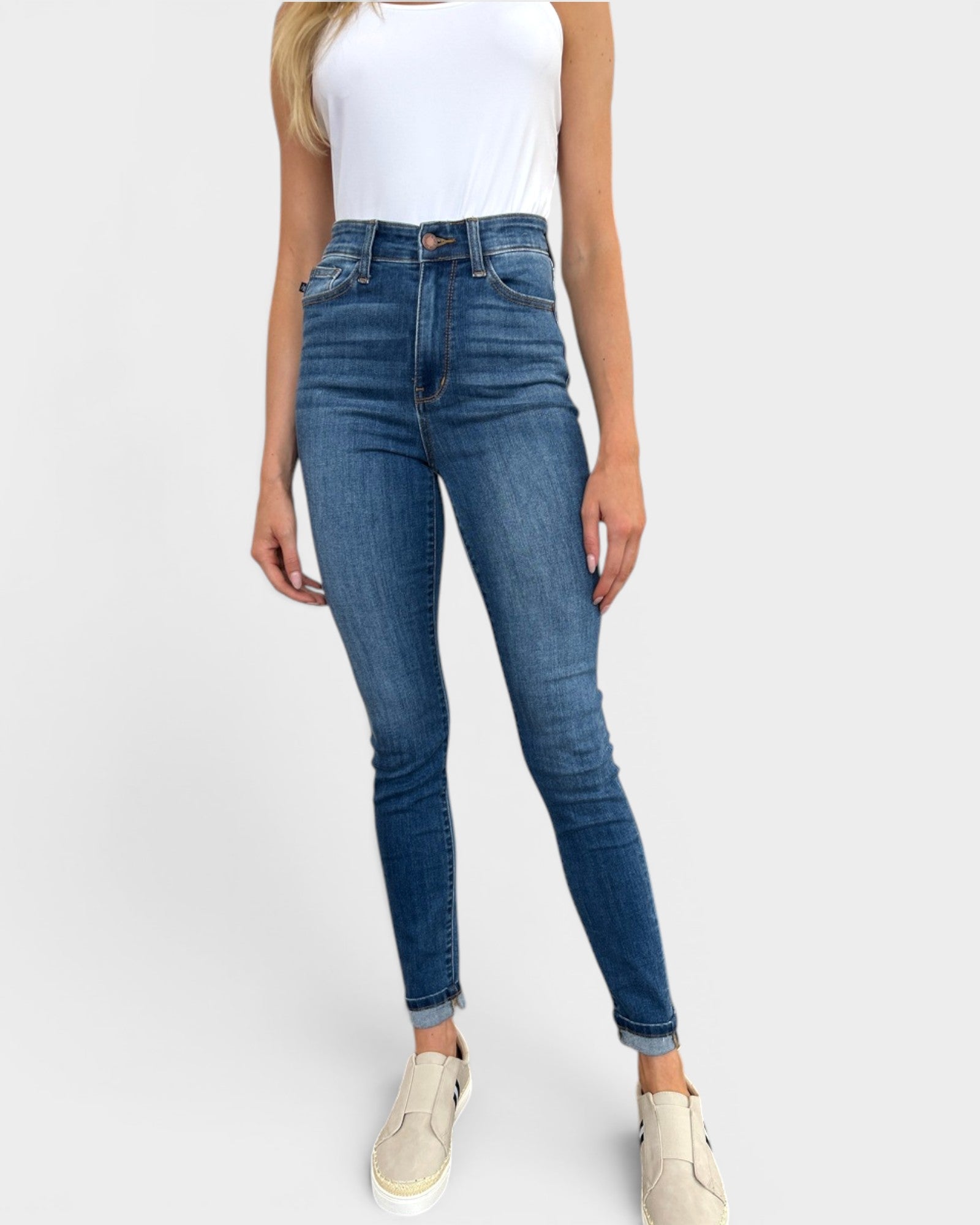 Person wearing blue jeans and a white top on a plain background