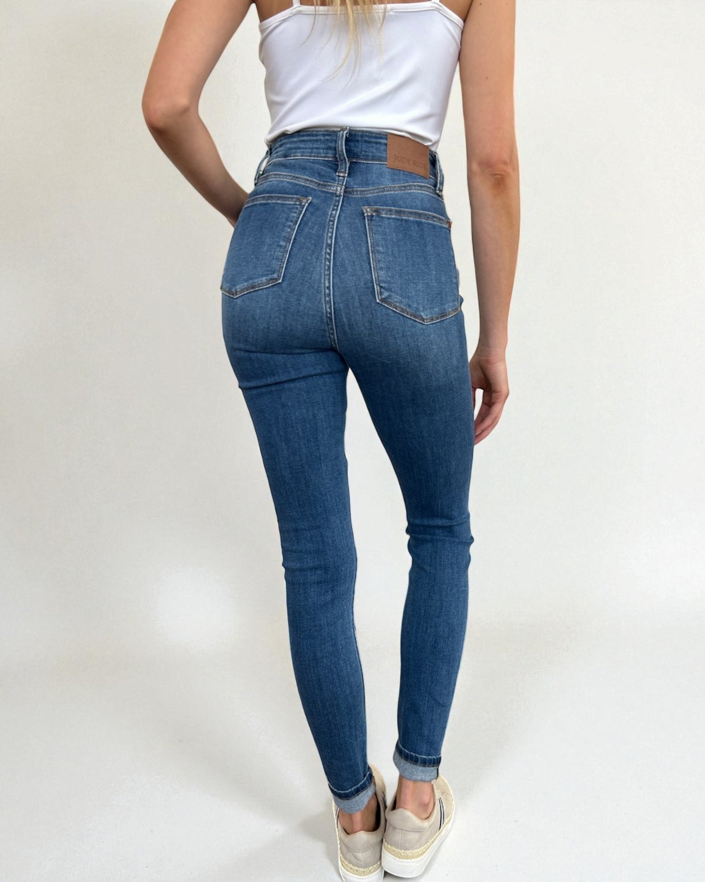 Person wearing blue jeans and a white top on a plain background